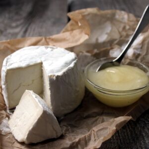 Close-up of gourmet soft cheese with a portion cut out, served with honey on rustic brown paper.